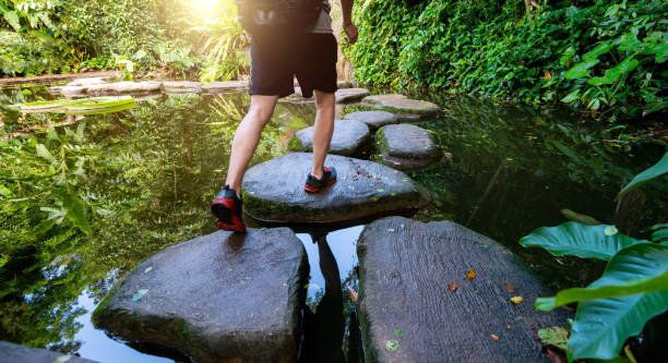 Male hiker crossing a river on stones